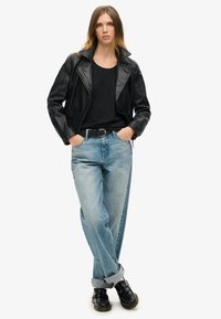 Zwarte leren motorjack over een zwart T-shirt, gecombineerd met lichtblauwe losse jeans en zwarte schoenen, met opgerolde mouwen.