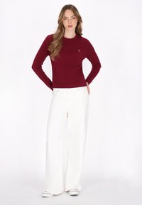 Bordeaux geribbelde gebreide trui met lange mouwen en ronde hals, gecombineerd met witte wijde broek en witte sneakers.