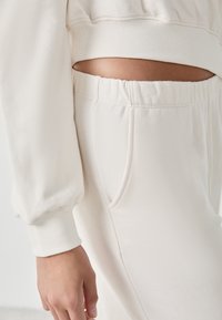Hellbeige Sweatshirt und passende Hose, mit gerippten Bündchen und Taschen. Der Stoff wirkt weich und strukturiert. Ausschnittdetails an der Taille.