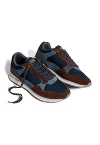 Zapatos deportivos que combinan materiales de ante y malla en azul marino, marrón y verde azulado, con una suela texturizada y cordones redondos.
