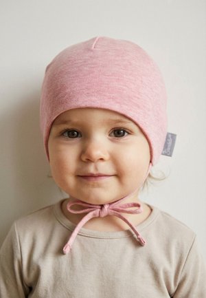 Toddler with brown eyes wearing a pink knit hat tied under the chin and a beige shirt, facing forward with a neutral expression.
