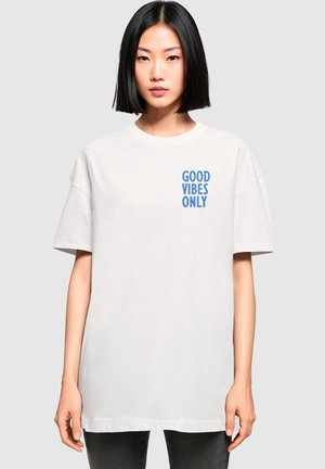 Hvit bomull T-skjorte med "GOOD VIBES ONLY" i blå tekst på venstre bryst. Avslappet passform med korte ermer og rund hals.