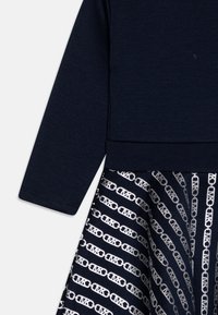 Marineblauw langemouwen top bevestigd aan een rok met een herhalend zilveren schakelpatternd met de initialen "MK".