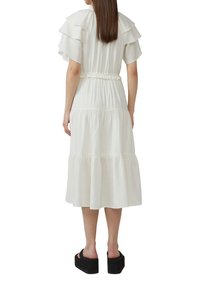 Witte, gelaagde midi-jurk met gerimpelde mouwen, een elastische taille en een vloeiende silhouet. Achteraanzicht toont de natuurlijke stofstructuur en gladde lijnen.