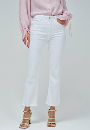 Jeans de mezclilla blanca acampanados de longitud corta, con un dobladillo sin rematar y bolsillos frontales, combinados con una blusa de botones rosa claro y tacones.