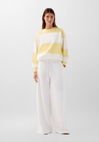 Felpa a righe gialle e bianche con maniche lunghe e collo rotondo, abbinata a pantaloni bianchi larghi con vita a coulisse.