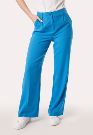 Felblau wijde broek met een gladde textuur, platte voorkant en een decoratieve knop, gecombineerd met witte sneakers.
