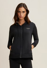 Sudadera negra con cremallera y capucha, con mangas largas y bolsillos. Fabricada en una tela suave, tiene un diseño minimalista con acentos de logo.