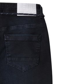 Donkerdenim jeans met een opvallende achterzak, slanke pasvorm en een wit label met tekst nabij de tailleband.