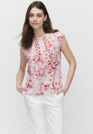 Blouse à imprimé floral en rose clair avec encolure plissée et manches courtes. Assortie à un pantalon blanc, offrant une coupe décontractée.