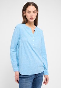 Helles blaues Langarm-Bluse mit rundem Halsausschnitt, Frontblende mit kleinen weißen Knöpfen und einem dezenten strukturierten Muster.