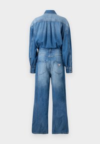 Combinaison en denim avec une coupe décontractée, col boutonné, manches longues et jambes larges. Dégradé de bleu clair à bleu foncé avec poches arrière et écusson logo.