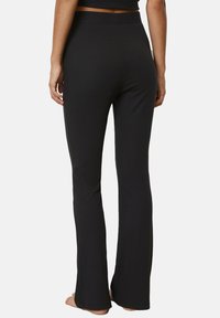 Zwarte flared broek gemaakt van zachte, rekbare stof; heeft een brede, elastische tailleband en een gladde textuur, aansluitend bij de heupen en bovenbenen.