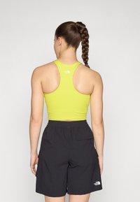 Crop top i lys gul med racerback-design och logotyp. Kombineras med svarta shorts med elastisk midja och sidficka.