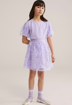 Rochie liliac cu mâneci bufante, stratificată cu un strat transparent brodat. Șosete mov deschis cu dungi albe și pantofi argintii sclipitori.