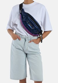 Marineblauwe puffer schoudertas met roze en zwarte gevlochten ritsdetails. Bevat een voorvak en een verstelbare zwarte strap. Gladde, glanzende verpakking.