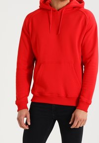 Czerwona bluza z kapturem z kieszenią kangurką, sznurkami, ściągaczami na rękawach i u dołu. Wykonana z miękkiego materiału o gładkiej fakturze, z rękawami raglanowymi.