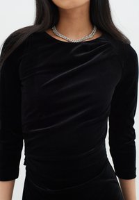 Černý sametový top s dlouhými rukávy a přiléhavým střihem, s kulatým výstřihem a jemnou texturou, doplněný stříbrným řetízkem.