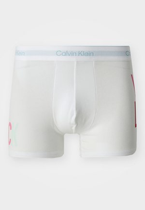 Valkoiset puuvillabokserit, jotka istuvat tiukasti. Vasemmalla puolella on punainen ja vihreä "YUCK" -teksti ja sininen Calvin Klein -brändätty vyötärö.