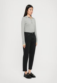 Polo grigio a maniche lunghe con colletto giallo e tre bottoni, abbinato a jeans neri a vita alta e mocassini neri.