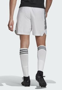 Witte sportshorts met zwarte zijstrepen, gecombineerd met knie-hoge witte sokken met drie zwarte strepen en zwarte voetbalschoenen.