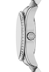 Srebrny zegarek z zaokrągloną kopertą, ozdobiony rzędem przezroczystych kryształków wzdłuż krawędzi. Posiada teksturowany przycisk boczny z logo MK.