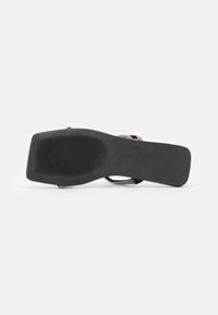 Talpă de sandală neagră, design plat cu suprafață texturată. Bretele subțiri, împletite din argint pentru ajustare. Stil minimalist, însoțită de o pernuță neagră netedă.