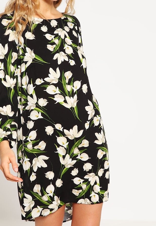Robe noire avec motif floral blanc, agrémentée de touches vertes. Manches longues, coupe ample, encolure ronde et longueur mi-cuisse.