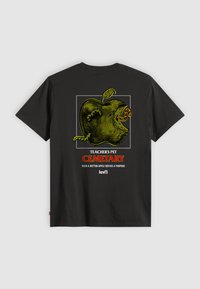 Sort t-shirt med et gult æblemotiv med orme, omgivet af teksten "TEACHER'S PET CEMETARY" og "selv et rådnet æble har en mening."
