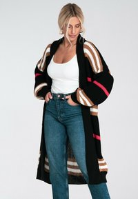 Sweter dziany w kolorze czarnym z brązowymi, białymi i różowymi pasiakami. Długi, luźny krój z szerokimi rękawami i otwartym przodem, połączony z spodniami o wysokim stanie.