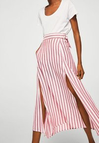 Jupe midi rayée rouge et blanche, dotée d'une fente haute de chaque côté et d'une taille ceinturée. Fabriquée en tissu léger avec un design fluide.