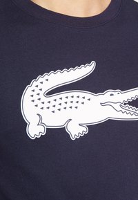 Marinblå T-shirt med en stor vit krokodilgrafik som har triangulära mönster på kroppen, rund halsringning och korta ärmar.