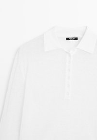 Polo blanc à manches longues avec col et cinq boutons, montrant la partie haute avant et l'étiquette du col.