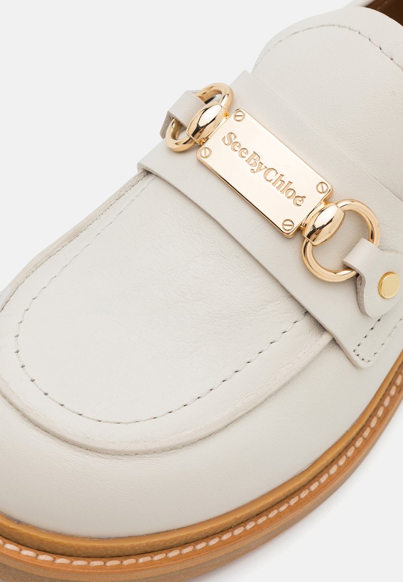 Beige Lederloafer mit goldfarbener Hardware, die mit einer rechteckigen Platte verziert ist, auf der "SeeByChloé" eingraviert ist, und einer kontrastierenden genähten Sohle.