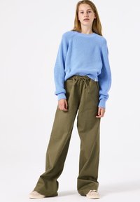 Lichtblauwe geribde trui met lange mouwen, gecombineerd met olijfgroene wijde broekspijpen, voorzien van een verstelbare trekkoord taille en beige schoenen.