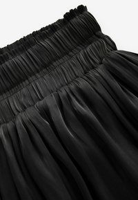 Jupe noire plissée avec une texture douce et fluide. Présente une taille smockée pour un peu d'élasticité et un aspect superposé.