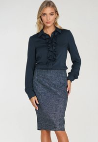 Ciemnoniebieska bluzka z falbaniastym detalem z przodu, w połączeniu z szaro wzorzystą spódnicą o kroju ołówkowym sięgającą do kolan. Gładka tkanina z dopasowanym krojem.