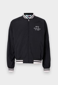 Sort bomberjakke med hvide striber på manchetterne og kanten, med broderet "NYC" og "Tommy Jeans est. 1985" logo.