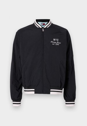 Jachetă bomber neagră cu accente albe pe manșete și tiv, având un logo brodat cu „NYC” și „Tommy Jeans est. 1985”.