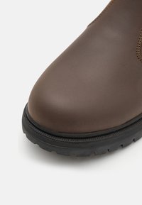 Brązowy skórzany but z okrągłym noskiem, teksturowaną czarną gumową podeszwą oraz widocznym przeszyciem wzdłuż górnej krawędzi.