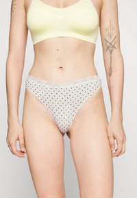 Lichtroze tang met stippen en kanten rand bij de taille. Heeft een gladde textuur en een ondeugende snit voor minimale bedekking.