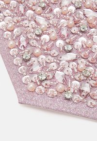 Rosa glittrande tyg dekorerat med paljetter, pärlor och ädelstenar i varierande former och storlekar, vilket skapar en texturerad och dekorativ yta.
