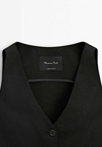 Zwart mouwloos vest met een V-hals, gemaakt van een textuurstof. Heeft een enkele knoopsluiting en een merklabel aan de binnenkant.