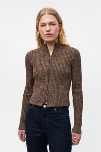 Ruskea, ribbineulottu vetoketjullinen neuletakki, jossa on korkea kaulus ja pitkät hihat, yhdistetty tummansinisiin farkkuihin. Kankaan pinta on teksturoitu ja saumat ovat tasaiset.