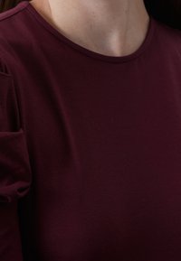 Burgundy t-shirt gjord av mjukt tyg, med en klassisk rund halsringning och insamlade kortärmar, med en slät yta.