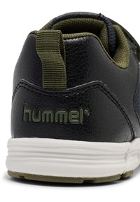 Svart syntetisk sneaker med olivgröna accenter, med en texturerad läderfinish, dragloopp och vit sula med mönstrat grepp.