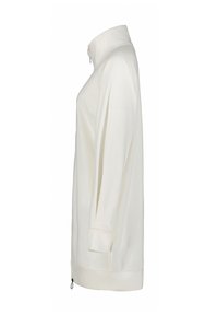 Pull à manches longues de couleur crème avec col montant et détail zip au bas de l'ourlet, vu de côté.