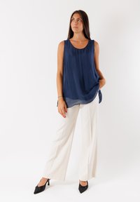 Blusa senza maniche blu navy in tessuto leggero, abbinata a pantaloni bianchi a gamba larga e décolleté neri a punta. Design semplice e fluido.