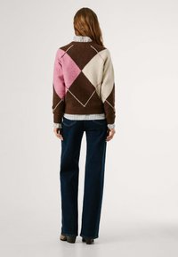 Bruine, roze en crème argyle-patroon trui in een zachte wolmix, gedragen over een licht geruit overhemd, gecombineerd met donkerblauwe wijde broek.