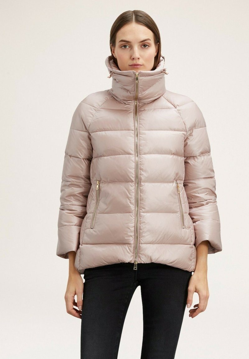 Jacket puffer roz deschis cu guler înalt, cusături verticale, fermoare aurii și două buzunare laterale. Prezintă mâneci lungi cu o croială relaxată.